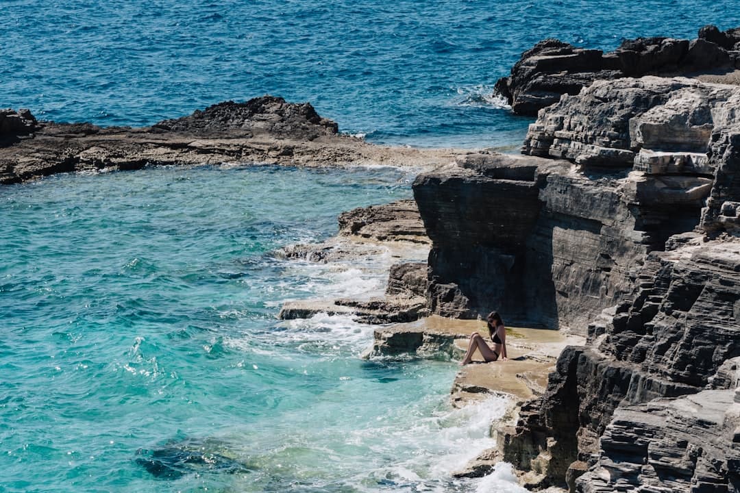 A small rocky outcrop drops into glass-clear turquoise water — the kind of pebble cove that defines Cape Kamenjak's coastline.