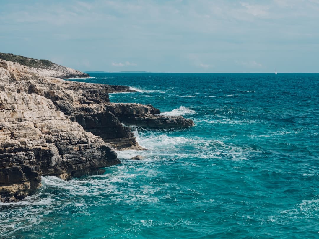 A green-topped limestone headland drops into turquoise Adriatic water at Cape Kamenjak.