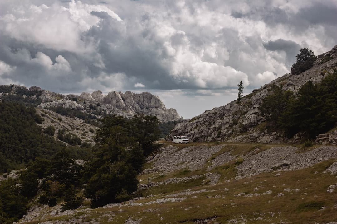 A walker on a stony Velebit trail with pine forest below and bare ridges above — the mid-altitude scenery on the way to Vaganski vrh.