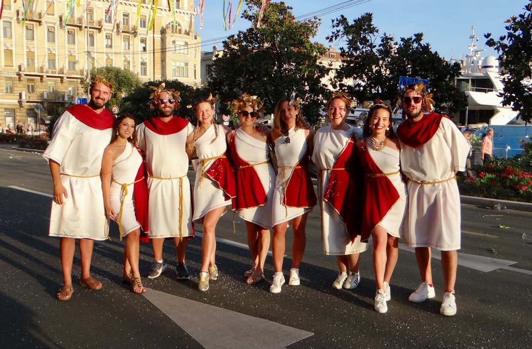 Un gruppo di mascherati in tuniche bianche con fasce rosse posa sul Korzo durante il corteo del Carnevale di Rijeka.