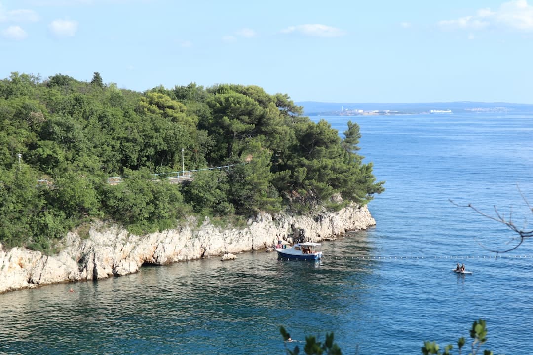 Una piccola barca riposa su acque calme sotto una bassa scogliera istriana — visitare Capo Kamenjak in barca evita del tutto la tariffa d'ingresso.