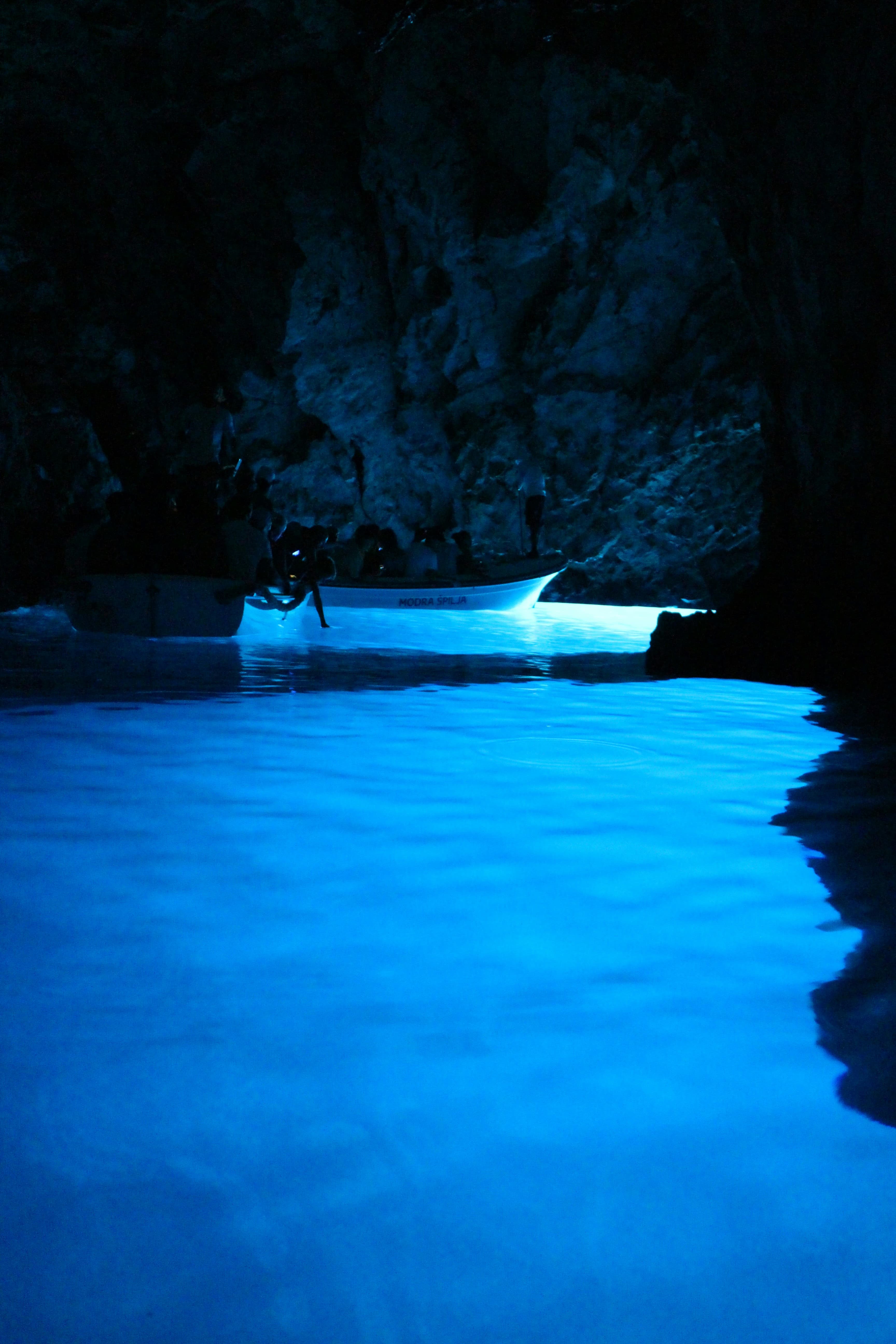 Türkisfarbenes Wasser am Eingang einer Mittelmeer-Meereshöhle mit einem kleinen Holzboot vor der Felswand — typisch für die Karstküste der Adria.