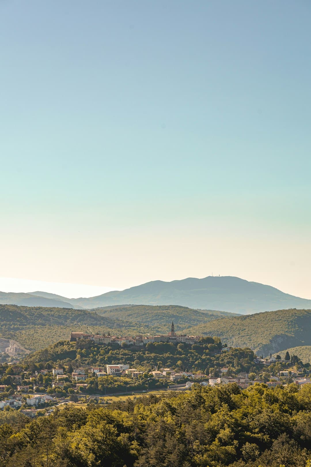 La città vecchia di Buzet incorona al tramonto un crinale boscoso sopra il bacino del Mirna — scenario della festa del tartufo di settembre.