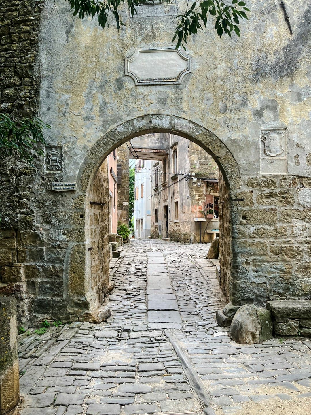 Un arco in pietra logorato dal tempo incornicia un vicolo selciato che sale a Grožnjan — il tipo di angolo silenzioso che definisce il borgo degli artisti.