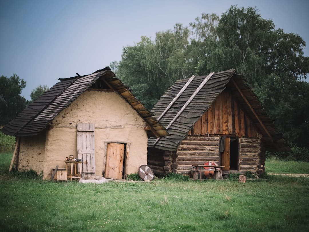 Two timber-built cottages with shingle roofs and covered porches set against a wooded backdrop, in the style of the protected Posavina houses at Krapje.