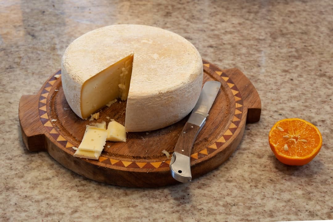 Ein kleiner gereifter Schafskäse-Laib auf einem Holzbrett mit ausgeschnittenem Stück, bereit zur Verkostung mit Obst.