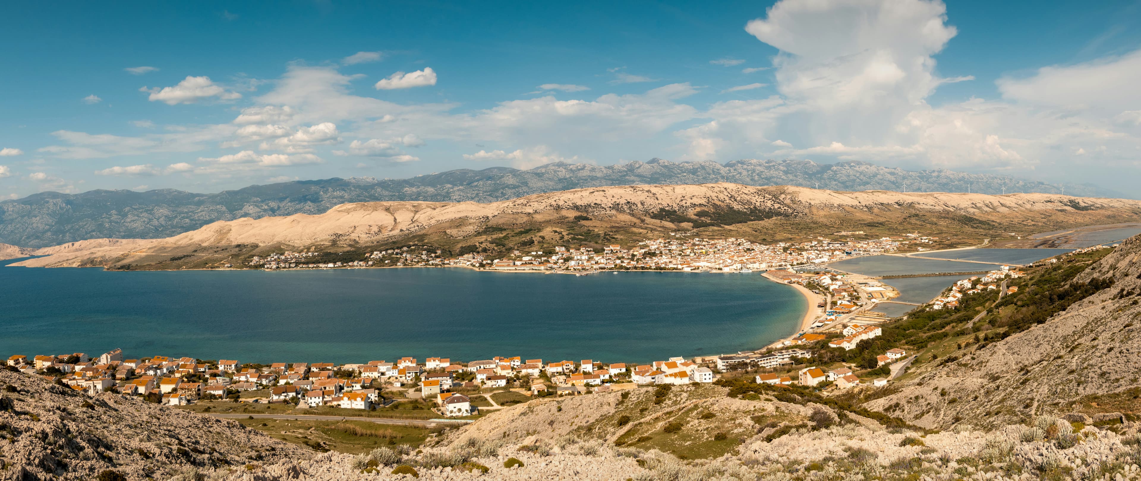 Blick über die Stadt Pag und ihren Hafen aus dem umliegenden weißen Karst, mit dem Velebit-Massiv jenseits des Kanals.