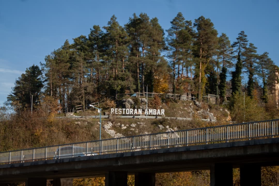 The approach bridge into Rastoke from the main D1 road, with the village name marked on the wooded ledge above.