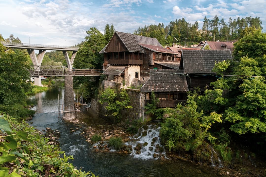 Wooden mill houses perched above the Slunjčica river in Rastoke, with the stone bridge of Slunj rising in the background.