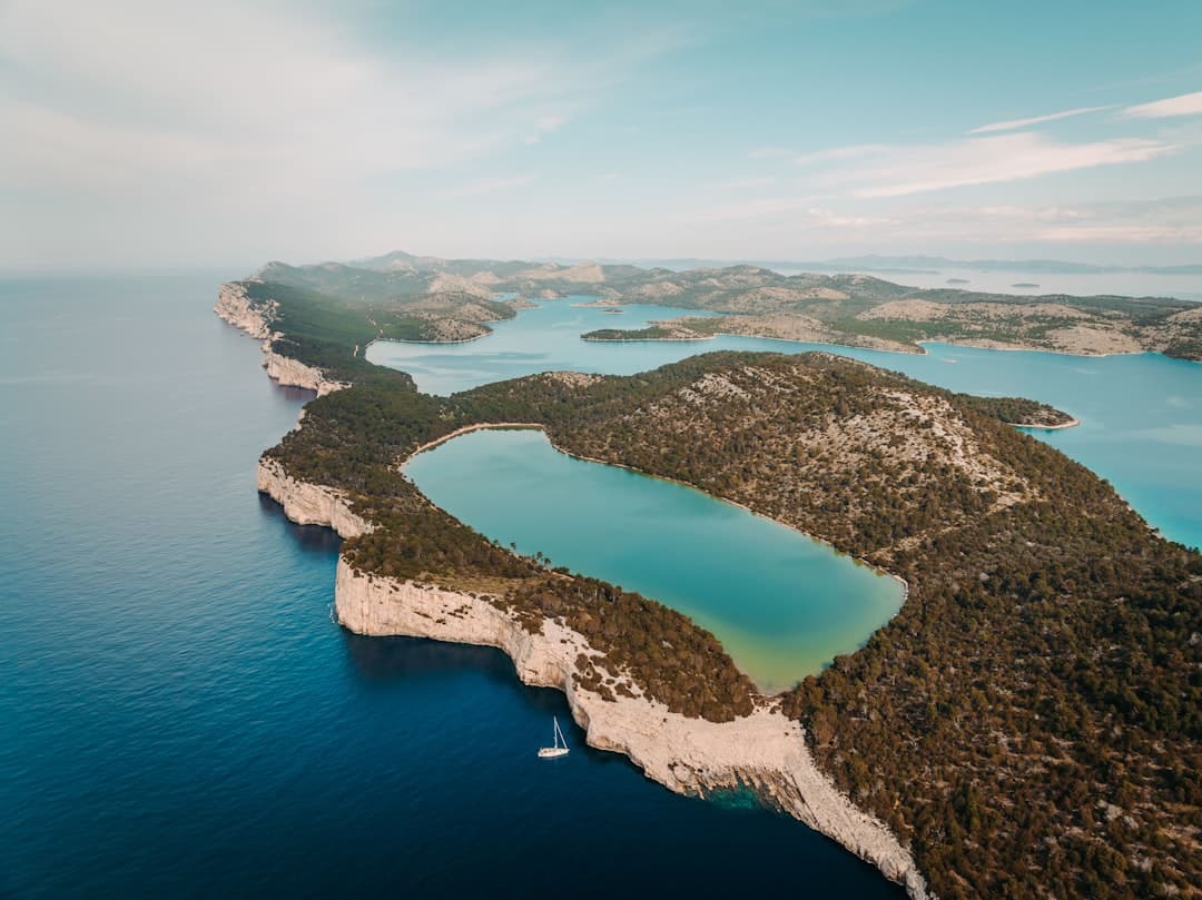 An aerial view of a sheltered inland saltwater pool ringed by white rock — evoking Lake Mir behind the cliffs of Telašćica.